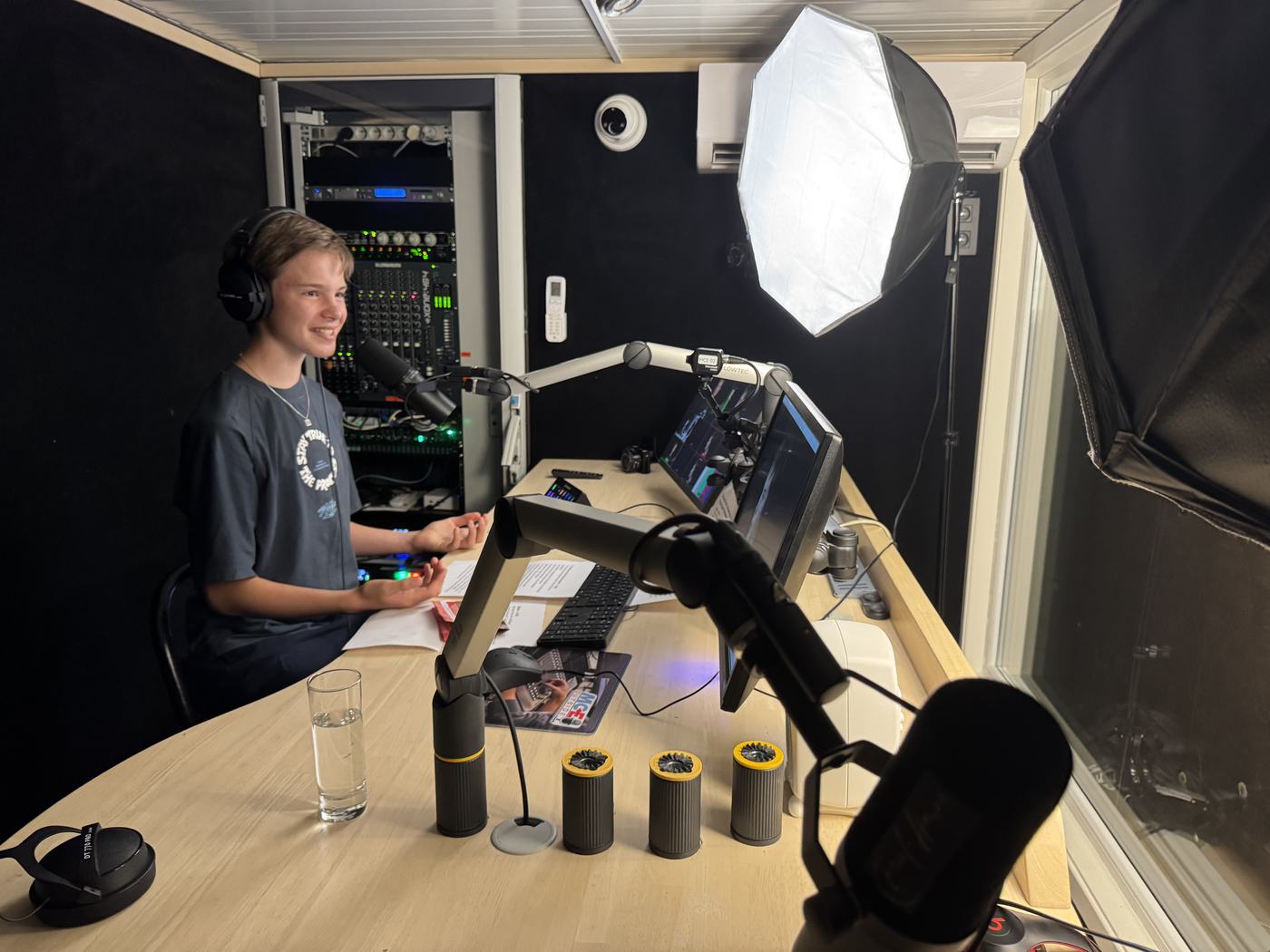 Emile-Henri aan de ronde tafel in de Podcastcontainer, met micro's, schermen, studiolampen en de mengtafel